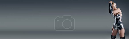 Téléchargez les photos : Futuriste femme particulière en tenue métallique regardant directement la caméra sur fond gris, bannière - en image libre de droit