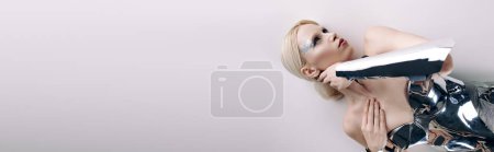 beautiful bizarre woman with blonde hair in silver futuristic attire lying on floor, banner