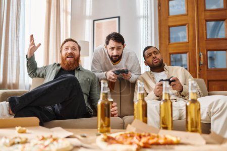 Three interracial handsome men in casual attire sitting on a couch, laughing, eating pizza, and drinking beer.