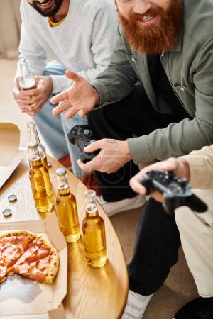 Dos hombres absortos en videojuegos, mientras disfrutan de la cerveza en un ambiente informal en casa, acompañados por su amigo interracial.