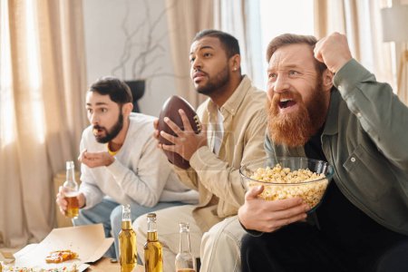 Three cheerful, diverse men in casual attire watching football and snacking on popcorn in a cozy setting.
