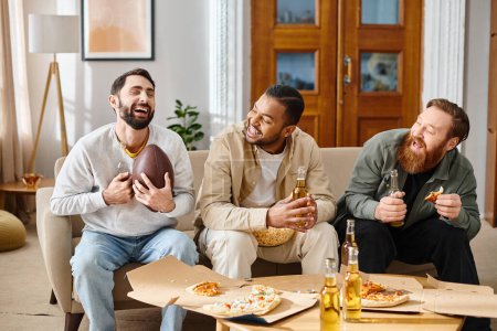 Three handsome, cheerful men of different races sit on a couch, enjoying pizza and beer in a casual home setting.