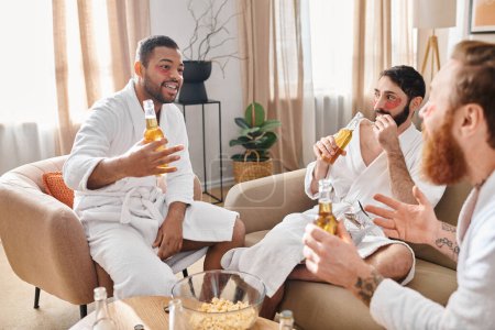 Three diverse cheerful men in bathrobes relax and have a great time together, sitting on top of a couch.