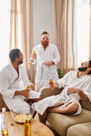 Téléchargez les photos : Trois hommes divers et joyeux en peignoirs profiter de la compagnie de l'autre dans un cadre confortable salon. - en image libre de droit