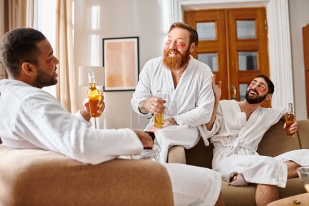 Three diverse, cheerful men in bathrobes laughing and chatting in a cozy living room setting.