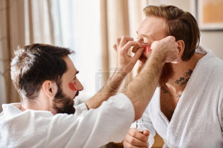 Two men in bathrobes are joyfully helping each other to put some eye patches.