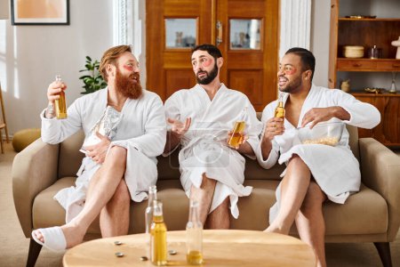 Three diverse, cheerful men in bathrobes, enjoying each others company as they sit on top of a couch.