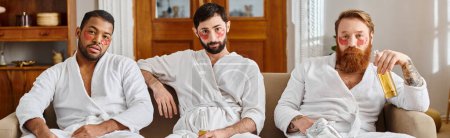 Photo for Three diverse, cheerful men in bathrobes sitting happily together on top of a couch. - Royalty Free Image