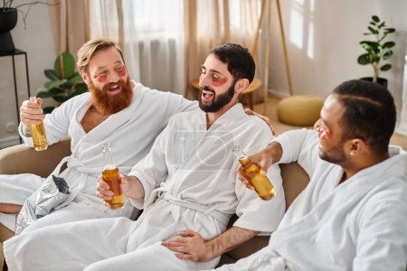 Three diverse, cheerful men in bathrobes enjoying a great time together while sitting on top of a couch.