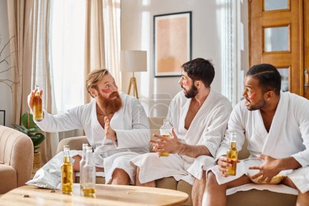 Three diverse, cheerful men in bathrobes sit, chat, and bond in a cozy living room setting.