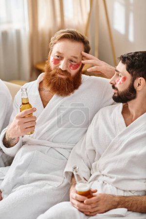 Two men in bathrobes, smiling, sit on a couch holding beer bottles, enjoying each others company and friendship.