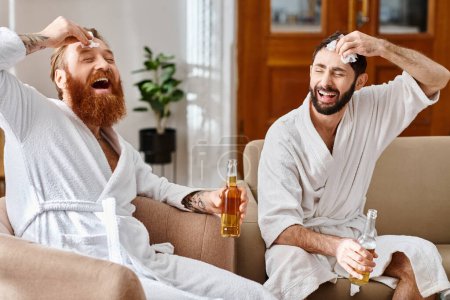Happy men in bathrobes laugh and chat while perched on top of a couch in a joyful moment of friendship.