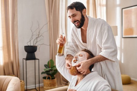 A man relaxes as his friend applies a facial mask, part of a spa experience shared by happy friends in bathrobes.