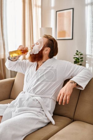 A man in casual attire sits comfortably on a couch, leisurely sipping on a beer.