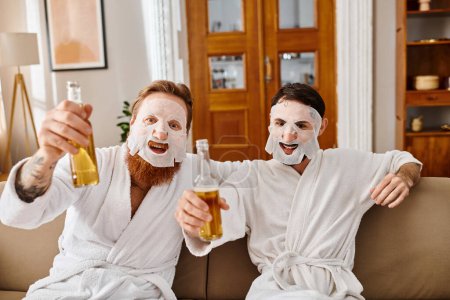 Two men in white robes share a fun moment, holding beer and wearing facial masks for a relaxing and enjoyable time together.