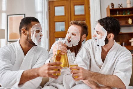 Three diverse men in bathrobes, masks on, enjoying beers together.