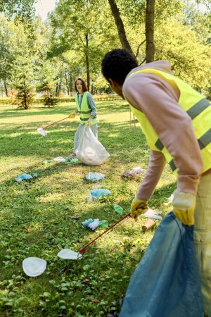 Diverse couple in a yellow safety vest clean a park together, reflecting their commitment to socially active volunteerism.
