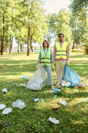 A socially active diverse couple in safety vests and gloves standing together in the lush green grass, cleaning the park.