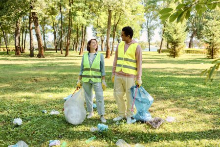 A loving, diverse couple in safety vests and gloves stands united, cleaning a park together.