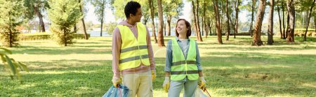 A socially active, diverse, loving couple in safety vests and gloves cleaning a park together, standing in the lush green grass.