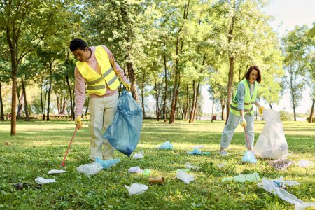 Gesellschaftlich aktives Paar mit Warnwesten und Handschuhen räumt mit einer Gruppe von Menschen Müll im Park auf.