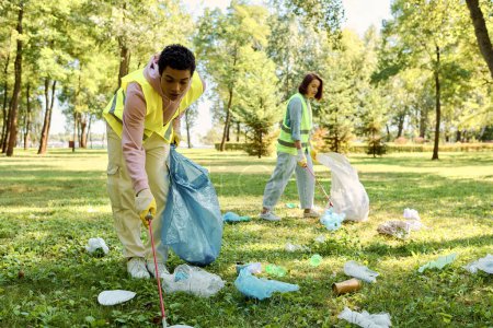 Diverse couple wearing safety vests and gloves cleaning park, standing in lush green grass with unity and love.