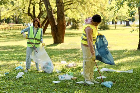 Un couple aimant et diversifié portant des gilets de sécurité et des gants debout dans l'herbe, nettoyant le parc avec soin et unité.