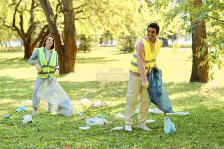 A socially active, diverse couple in safety vests and gloves stands in the grass, cleaning a park together with love and dedication.