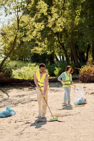 A socially active diverse couple in safety vests and gloves stands in the sand, embodying love and teamwork as they clean up the park.