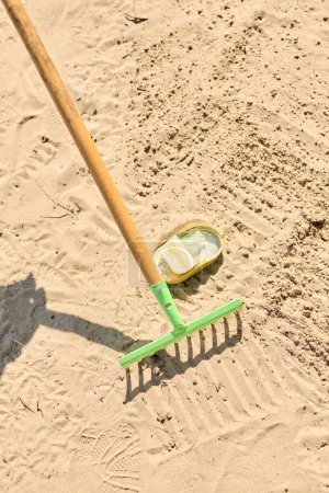 A shovel and a rake are peacefully resting on the sandy ground under the sun.