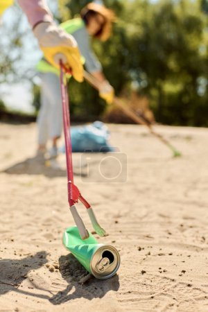 A woman in a safety vest and gloves diligently cleans the sand in a park while her partner assists, showcasing their dedication to cleanliness.