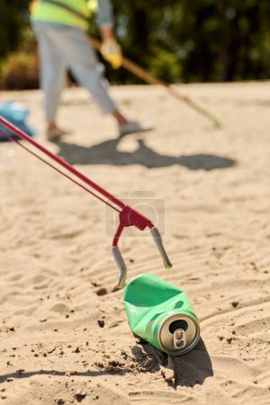 Una lata verde con una manija roja se sienta en una playa de arena, simbolizando la administración ambiental y los esfuerzos de limpieza de la playa.