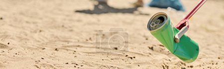 Téléchargez les photos : Une canette de soda pendue à une corde sur la plage, projetant des ombres ludiques dans le sable. - en image libre de droit