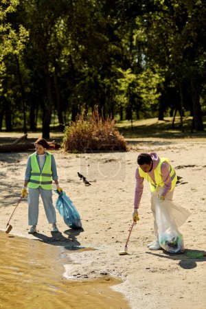 Ein sozial aktives, vielfältiges Paar in Warnwesten und Handschuhen, das im Sand steht und gemeinsam den Park säubert.