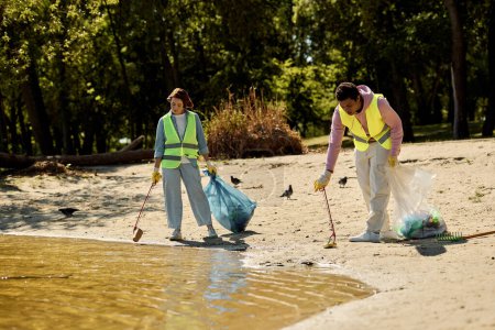 A socially active diverse loving couple in safety vests and gloves cleaning the park together while standing in the sand.