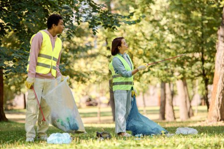Téléchargez les photos : A loving, diverse couple in safety vests and gloves stand side by side on lush green grass, engaged in park cleanup. - en image libre de droit