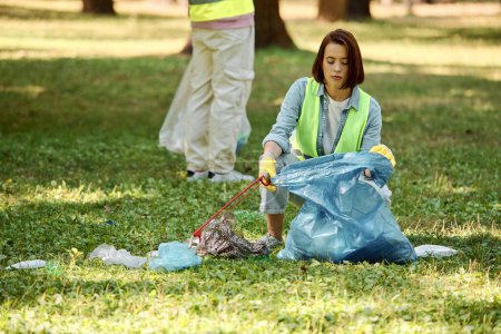 Foto de Pareja multicultural trabajadora y trabajadora que limpia apasionadamente un parque mientras usa guantes de seguridad. - Imagen libre de derechos