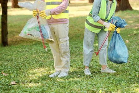 A socially active, diverse couple in safety vests and gloves cleaning a park together, standing in the lush green grass.