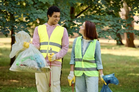 A loving couple, socially active and diverse, stands in the grass wearing safety vests and gloves, cleaning the park together.