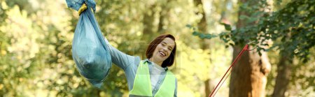 Téléchargez les photos : Une femme vêtue d'un gilet vert tenant un sac bleu, participant à une activité de nettoyage du parc avec son partenaire. - en image libre de droit