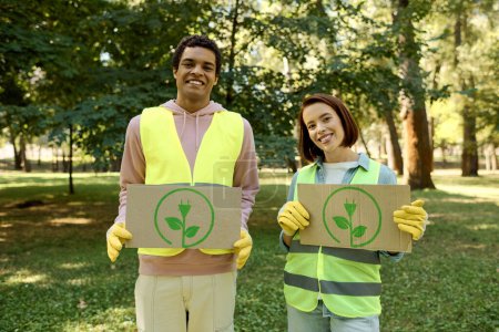 Photo for African american man and woman in safety vests holding up cardboard signs, advocating for a cause at a park cleanup event. - Royalty Free Image