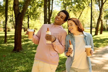 Una pareja diversa y cariñosa, vestida con trajes vibrantes, disfruta de un paseo pausado por un exuberante parque.