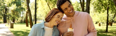 Téléchargez les photos : Un homme et une femme en tenue vibrante partagent joyeusement une bouteille de bière dans un parc, profitant mutuellement de la compagnie. - en image libre de droit