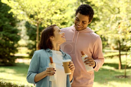 A stylish and diverse couple enjoying each others company while holding coffee cups in a vibrant park setting.