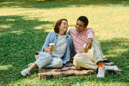 Téléchargez les photos : Un homme et une femme en tenue vibrante assis sur une couverture dans l'herbe, profitant mutuellement compagnie dans un cadre paisible de parc. - en image libre de droit