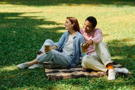 A diverse couple in vibrant attires sitting on a blanket in the grass, enjoying each others company.