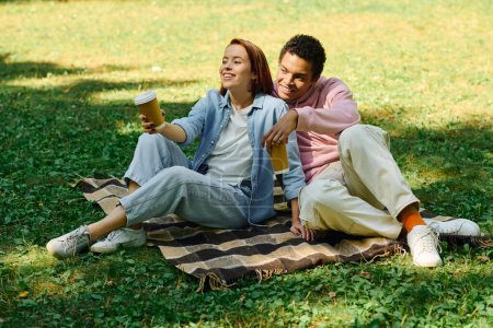 Un homme et une femme vêtus de vêtements vibrants assis sur une couverture dans l'herbe, profitant mutuellement compagnie dans un cadre de parc serein.
