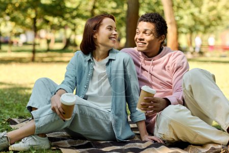 Téléchargez les photos : Un couple diversifié en tenue vibrante assis sur une couverture, profitant d'un moment paisible ensemble dans un parc. - en image libre de droit