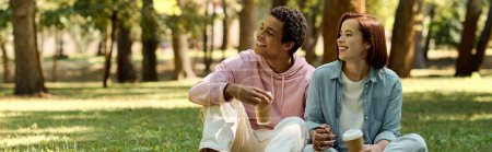 Téléchargez les photos : Couple diversifié en tenue vibrante profitant d'un moment paisible ensemble alors qu'ils sont assis sur l'herbe verte luxuriante dans un parc. - en image libre de droit