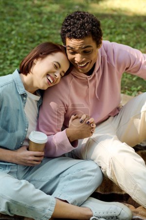 Téléchargez les photos : Un couple diversifié en tenue vibrante s'assoit paisiblement sur le terrain, profitant mutuellement de la compagnie dans un cadre de parc. - en image libre de droit
